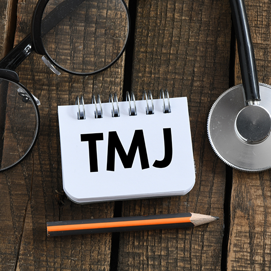 Notepad that says TMJ on desk with pencil glasses and stethoscope