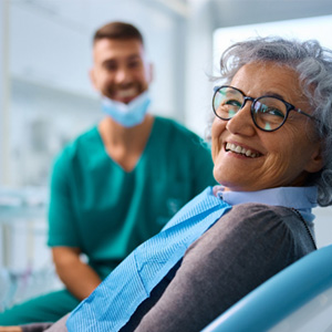 Woman with black glasses smiling while sitting in treatment chair